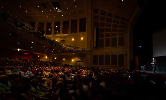 Photo of Alan Alda speaking to large crowed at UNCG Auditorium