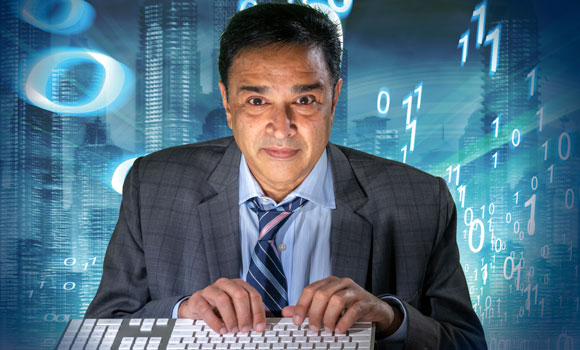 Professor Gupreet Dhillon with fingers on keyboard and math numbers behind him with blue background - like he's inside of a computer.