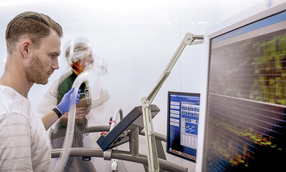 Photo of person running on treadmill while being hooked up to monitors and assessed by researcher
