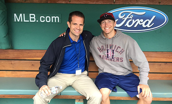 Two men pose for a photo in baseball dugout