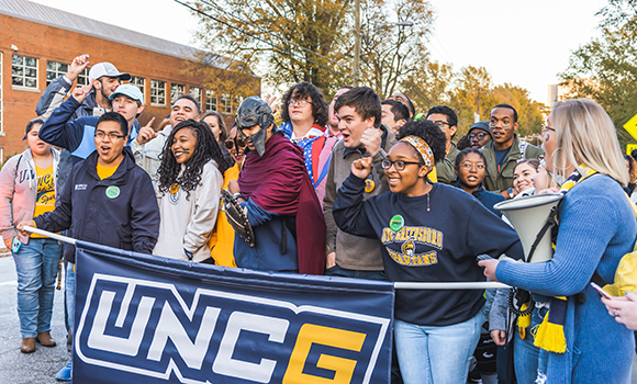 Students holding a UNCG banner and cheering while participating in Storm the Streets in 2018