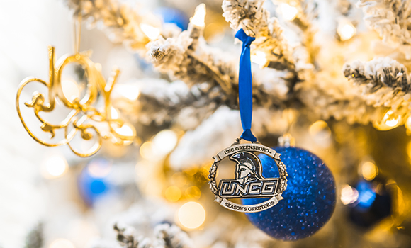 UNCG ornament hanging from a branch on a holiday tree.