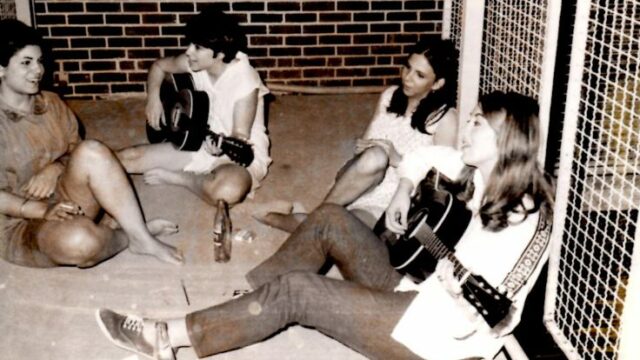 Picture of students sitting on pavement playing guitar and singing