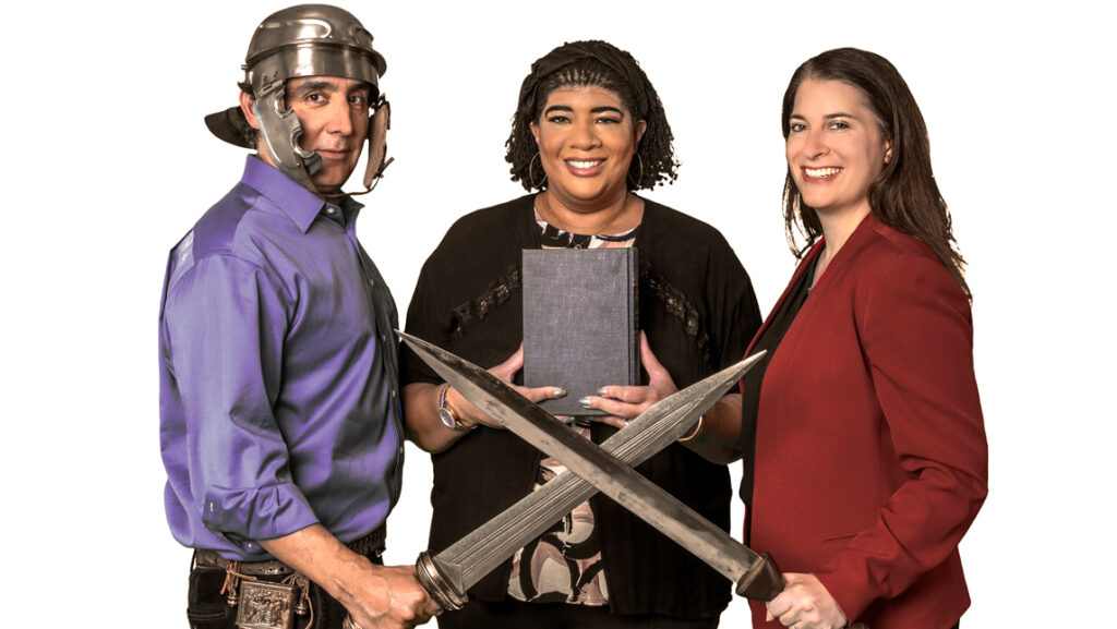 People posing with classical swords, helmets, a book.