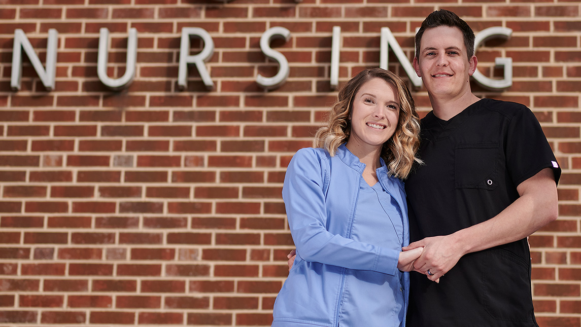 Portrait of Ben and Jordan Cassidy holding hands in front of School of Nursing building