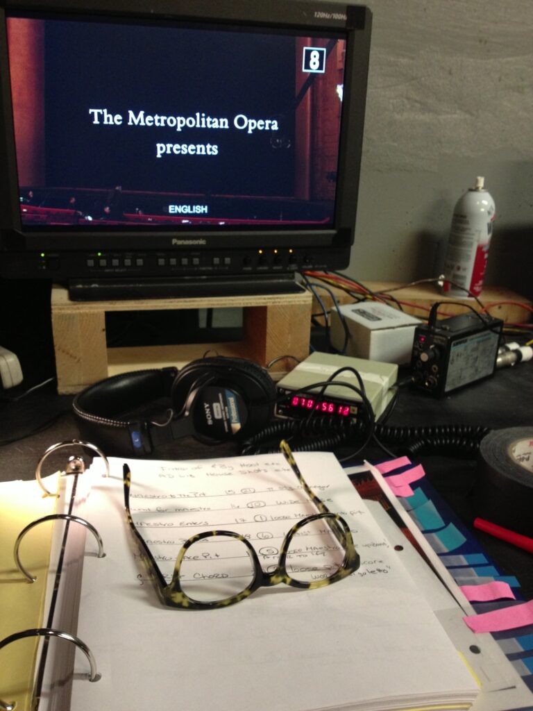 Photo of desk with notebook and glasses, among other supplies, and a TV