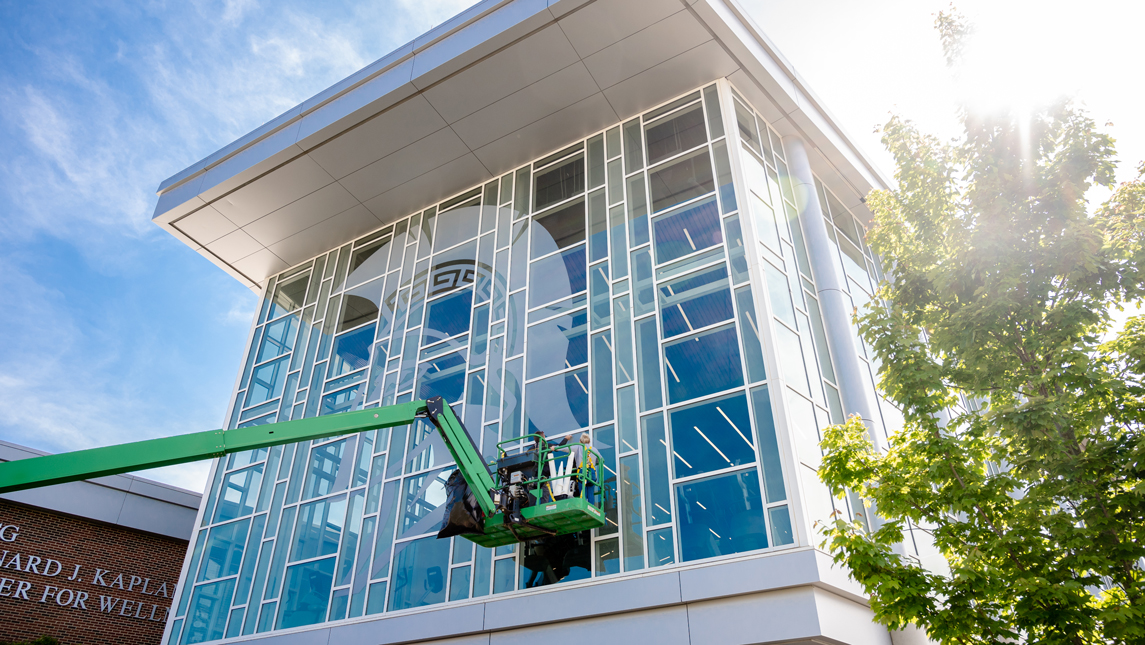 Workers on crane installing graphic on Kaplan glass exterior