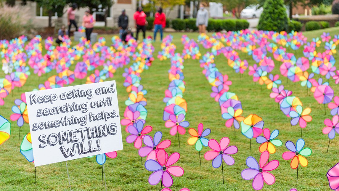 Pinwheel display with a sign that reads: "Keep asking and searching until something helps. Something will!"