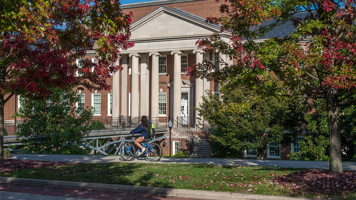 student riding bike with fall foliage and academic building