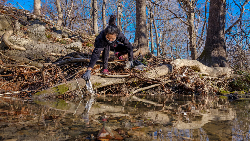Student picking up trash out of a creek