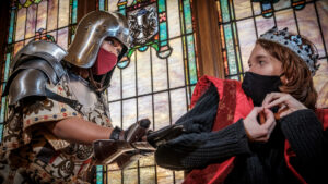 woman in helmet and man in crown engaged in action scene in church