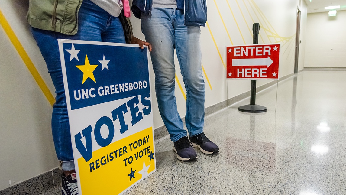 Students stand with sign that reads "UNC Greensboro VOTES; Register today to vote"