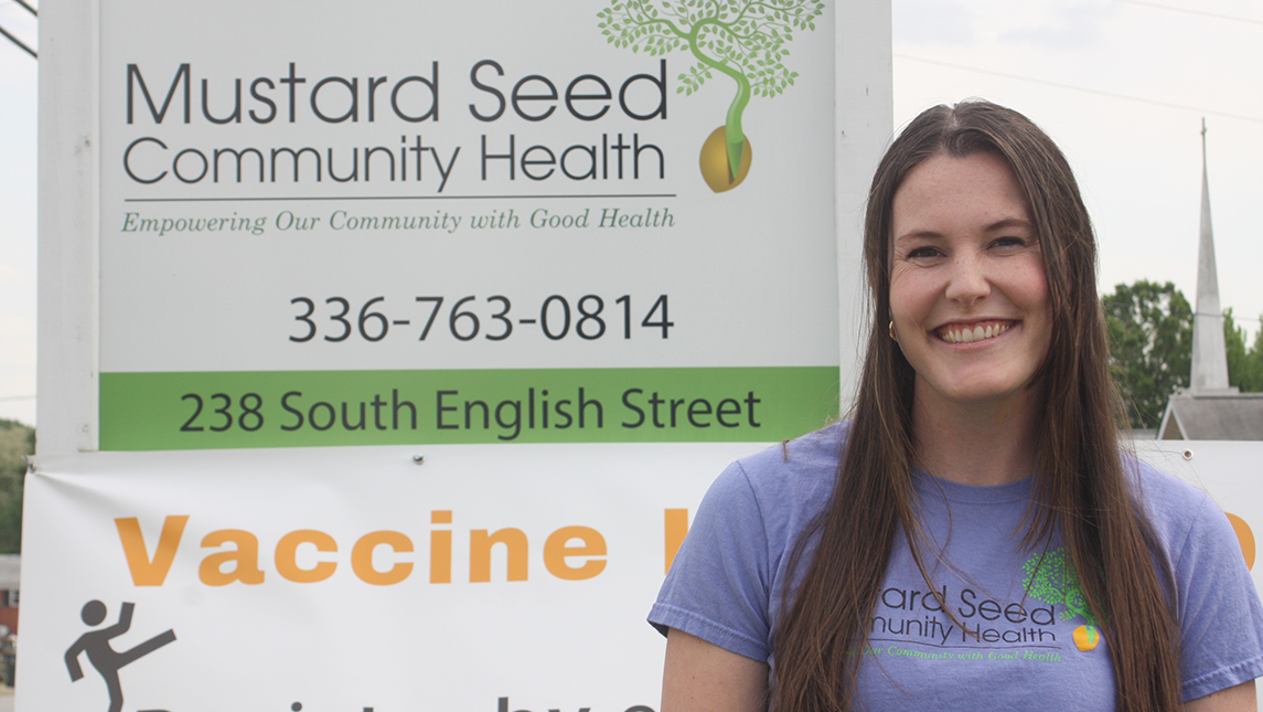 Caroline Wells smiling in front of "Mustard Seed Community Health" sign