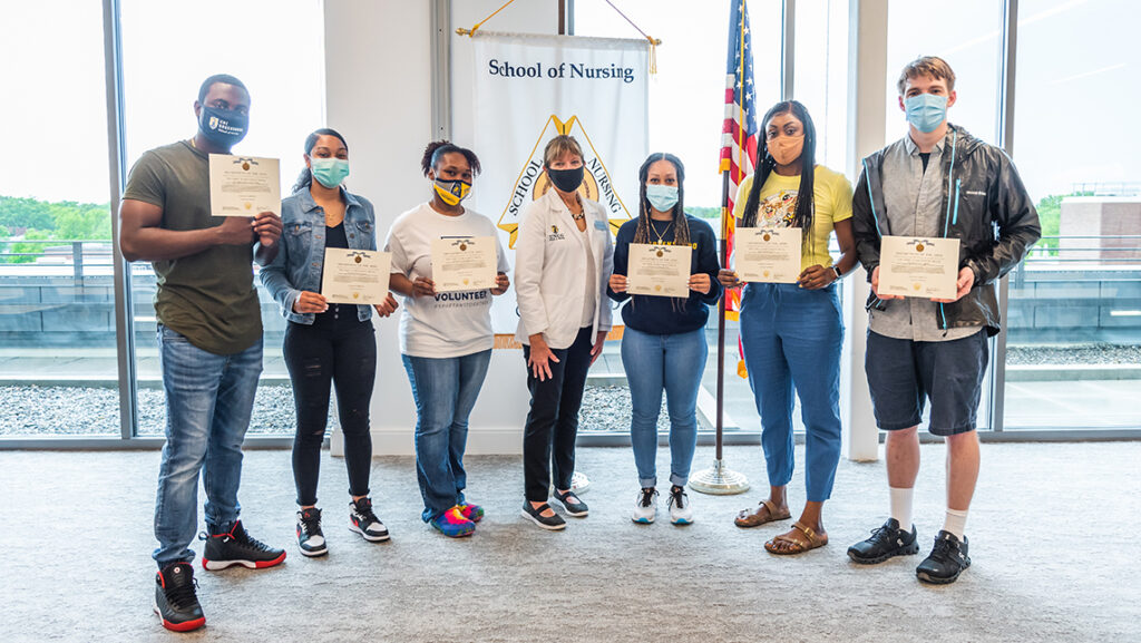 Group of students holding up diplomas with faculty member