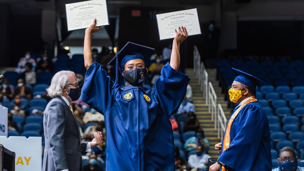 Student holding up two diplomas on stage at commencement