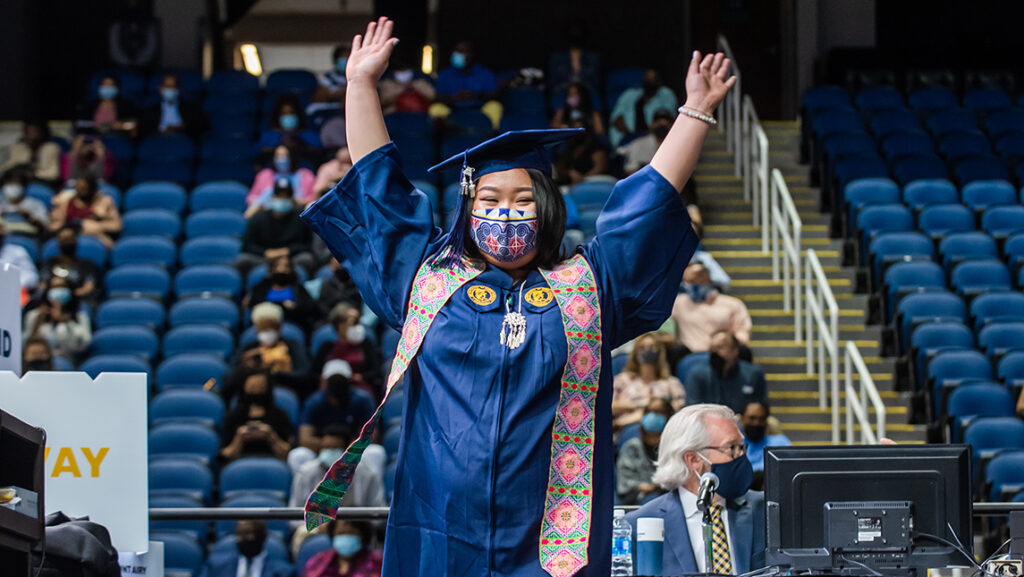 Student holding up hands in celebration at commencement