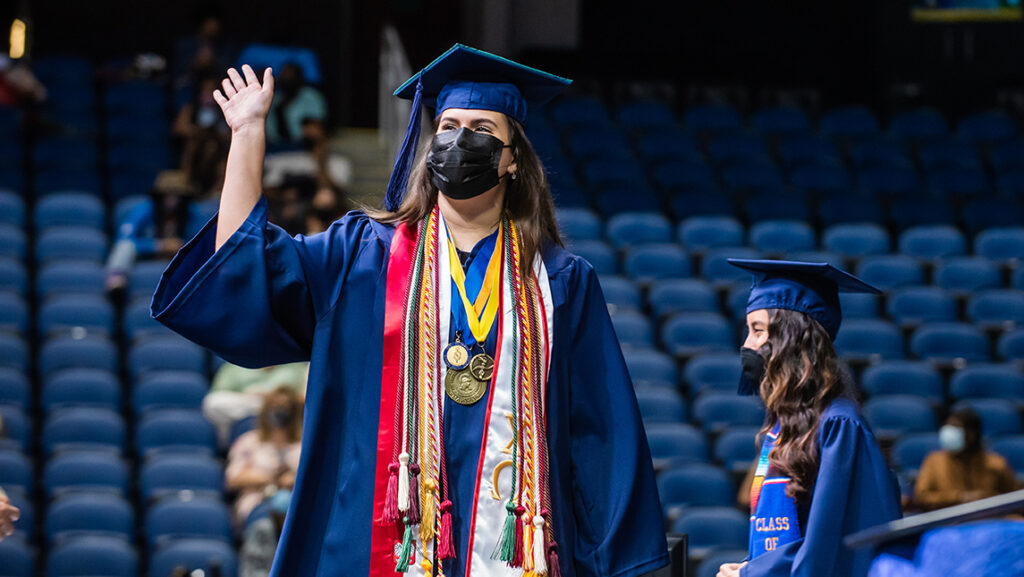 Student waving while crossing the stage on commencement