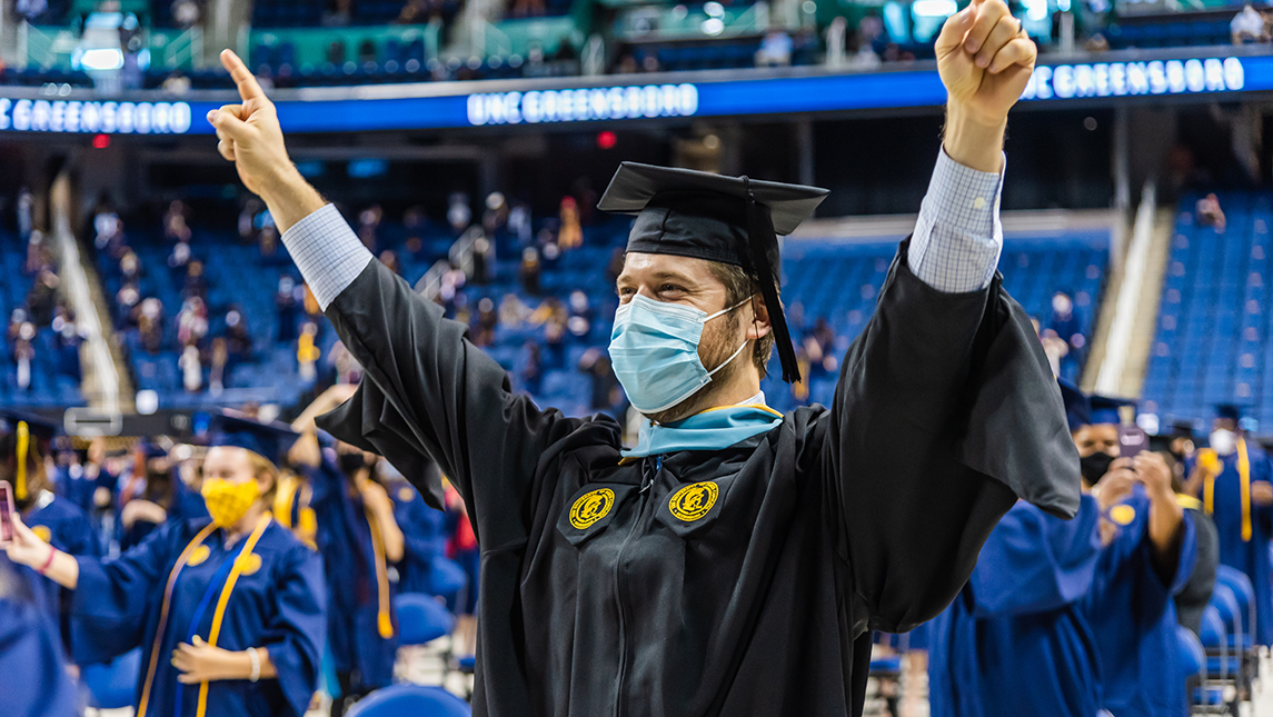Student holding up both hands in celebration at commencement