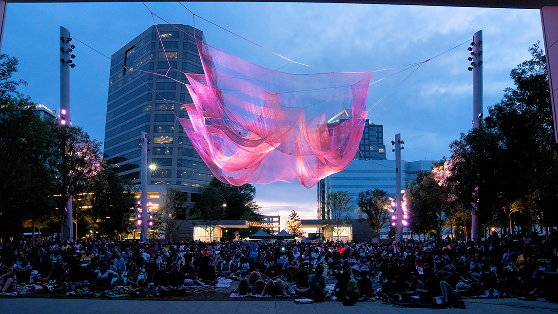 Crowd of people sitting underneath an art sculpture in Downtown Greensboro at night