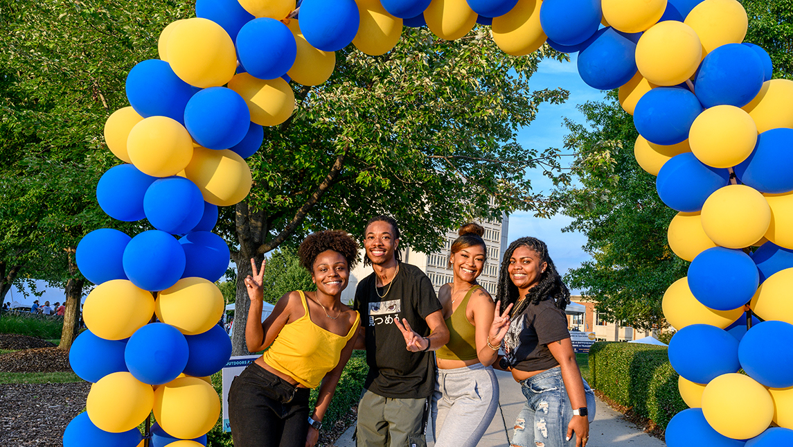 four students pose under a blue and gold balloon arch