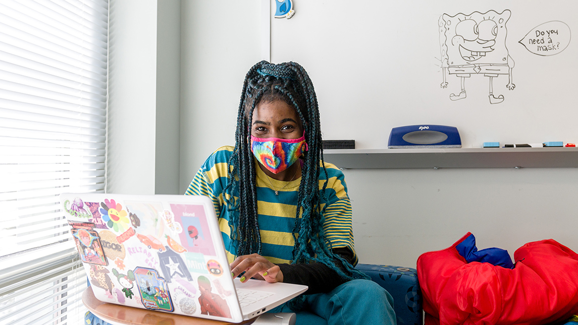 Student wearing a face covering while working on a laptop