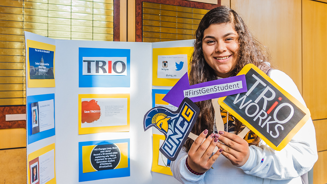 Student holding a UNCG sing, a #FirstGenStudent sign, and a Trio Works sign