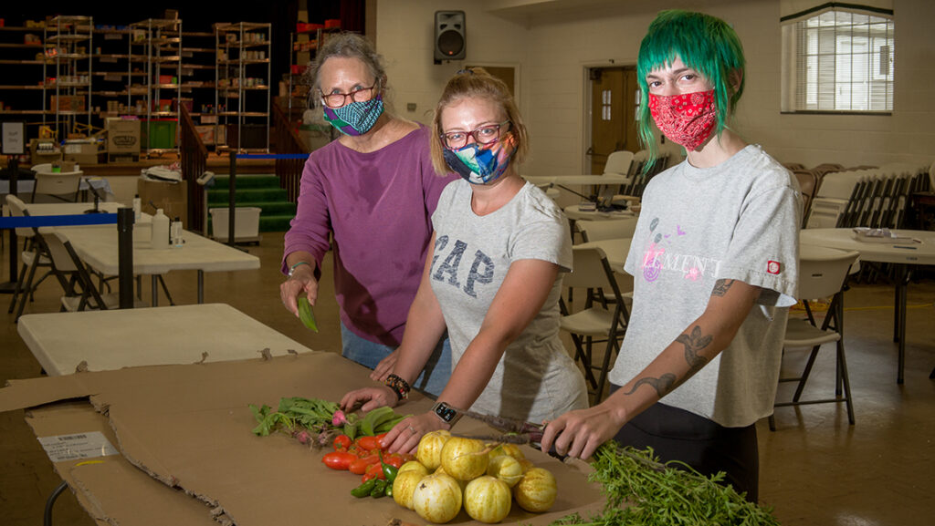 Two students a professor wearing face coverings at a table holding freshly picked vegetables inside Spartan Open Pantry