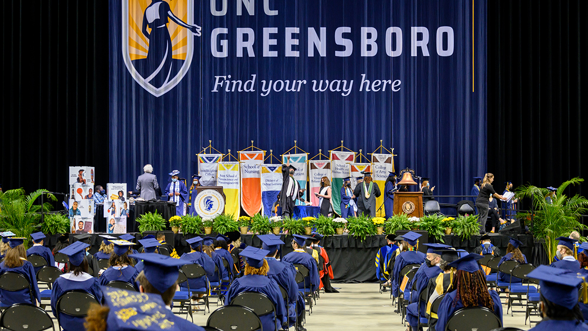 Wide shot of graduates seated and a student celebrating while walking across stage