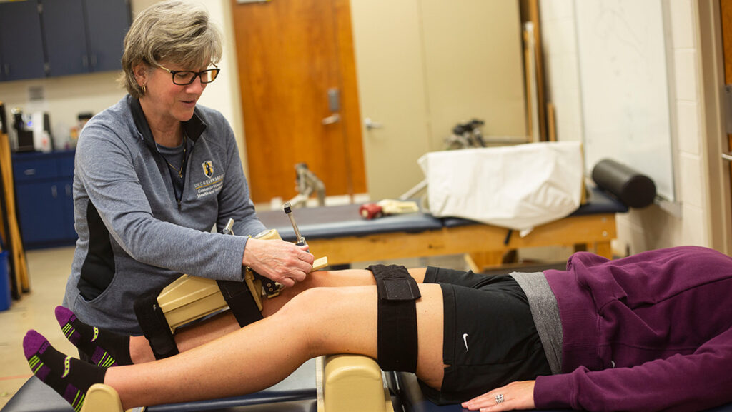 A woman uses a device to measure knee laxity on another women's knees