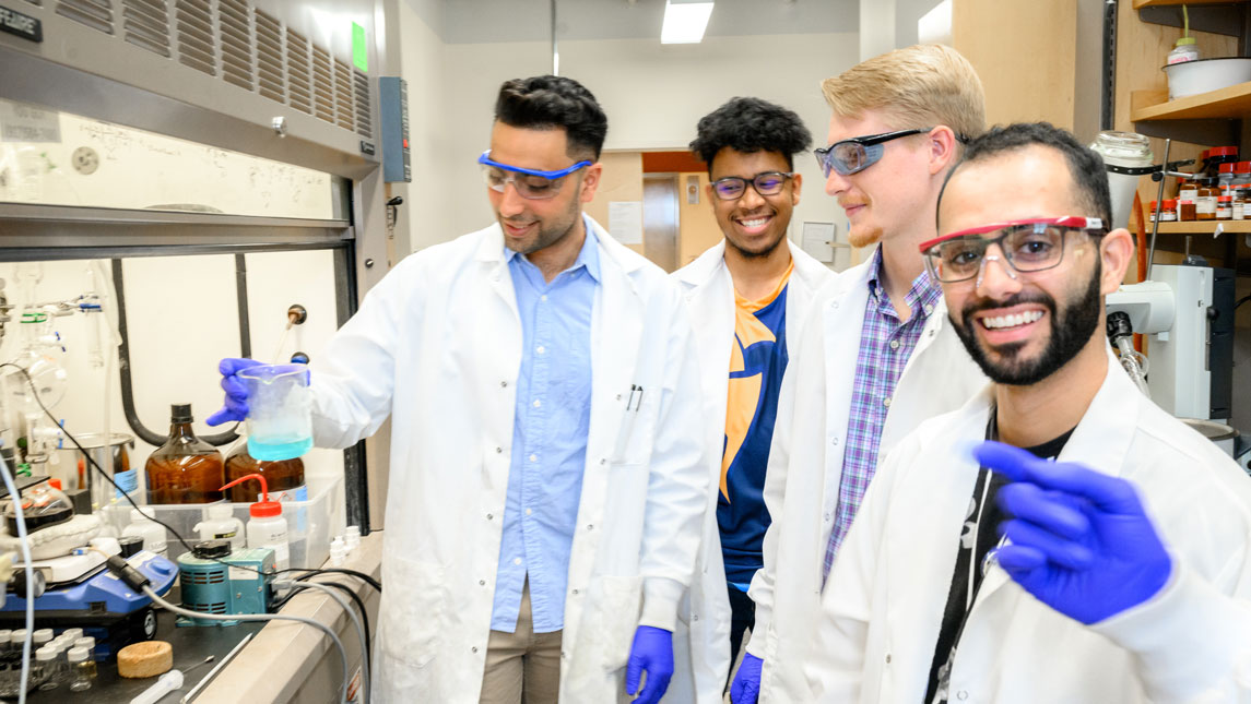 four scientists performing a reaction in a lab, smiling