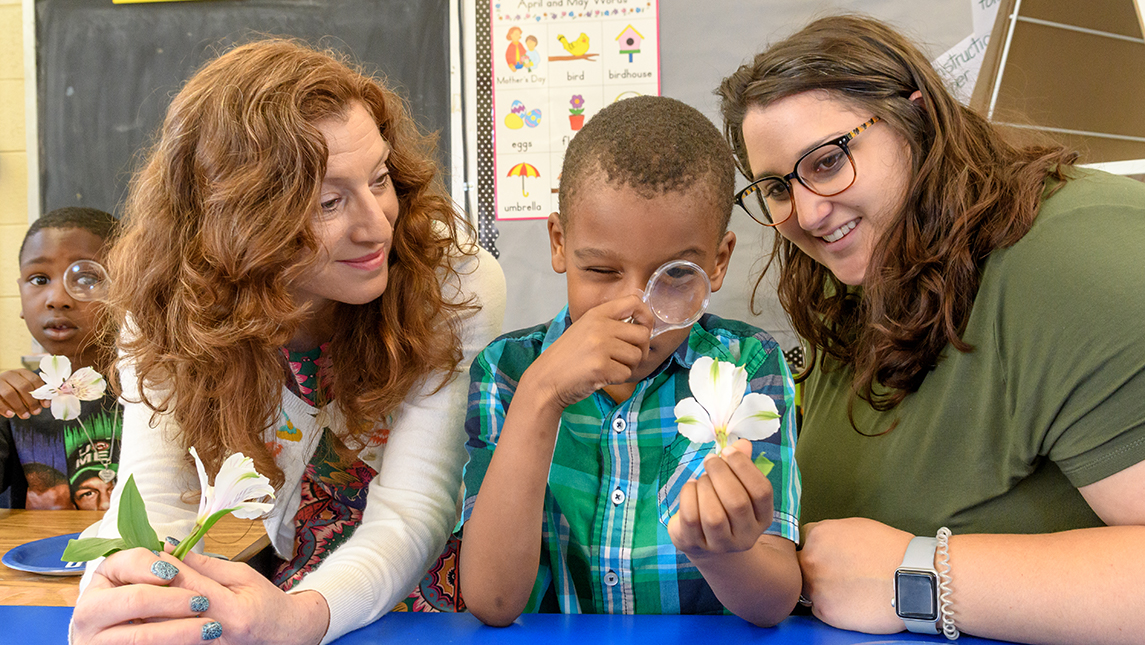 STEM Teacher Leader Collaborative Coach Dearing Blankmann with a School of Education doctoral student and first grade student looking at flowers