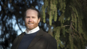 A man stands in front of a tree in formal clothing.