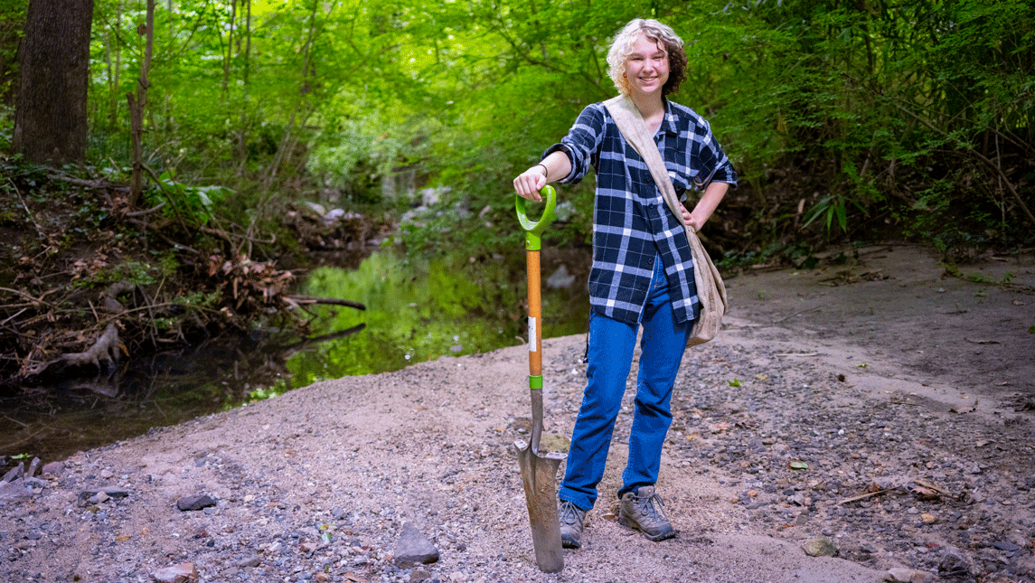 Student posing outside with a shovel