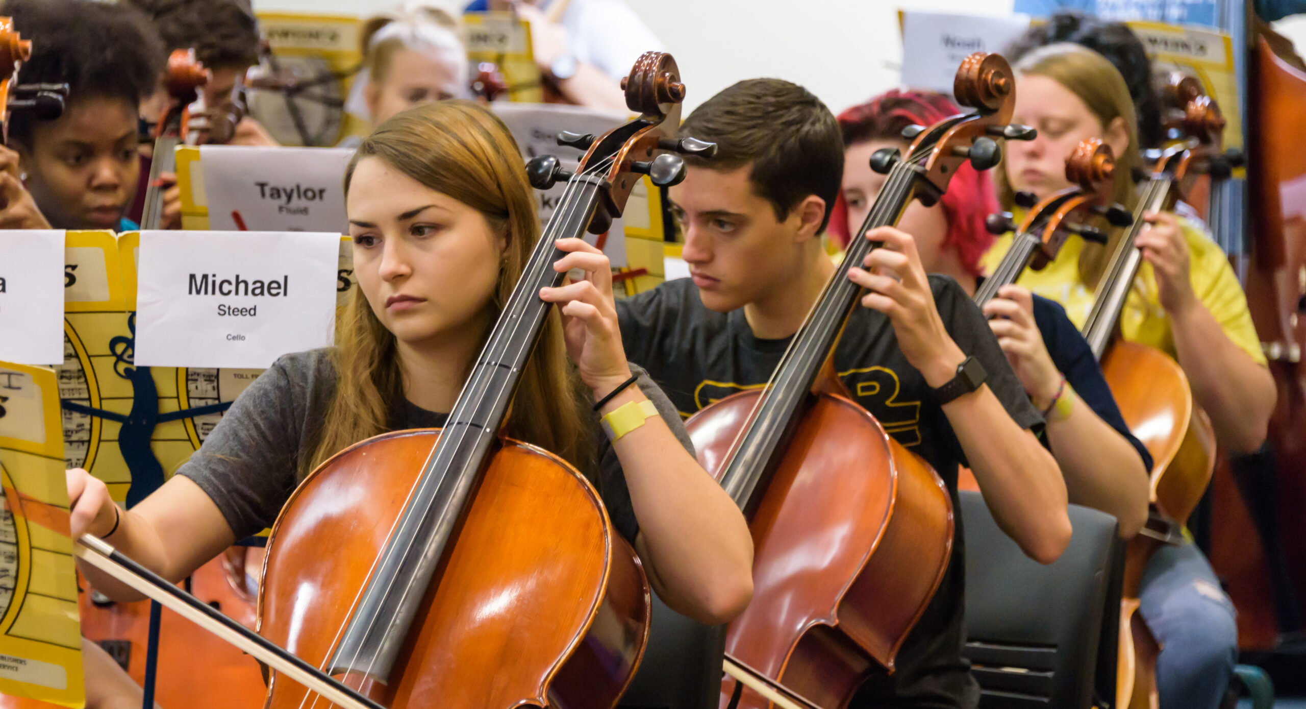 Four students playing cello in orchestra.