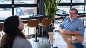 Tal Blevins sits at one of his restaurant tables talking to visitor Michael Ream.