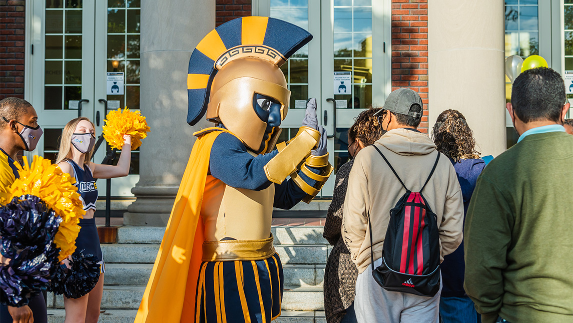 Spiro the mascot and UNCG cheerleaders wave to prospective students walking past.