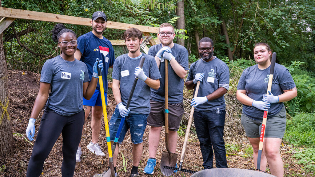 Six students stand in the middle of garden with spades.