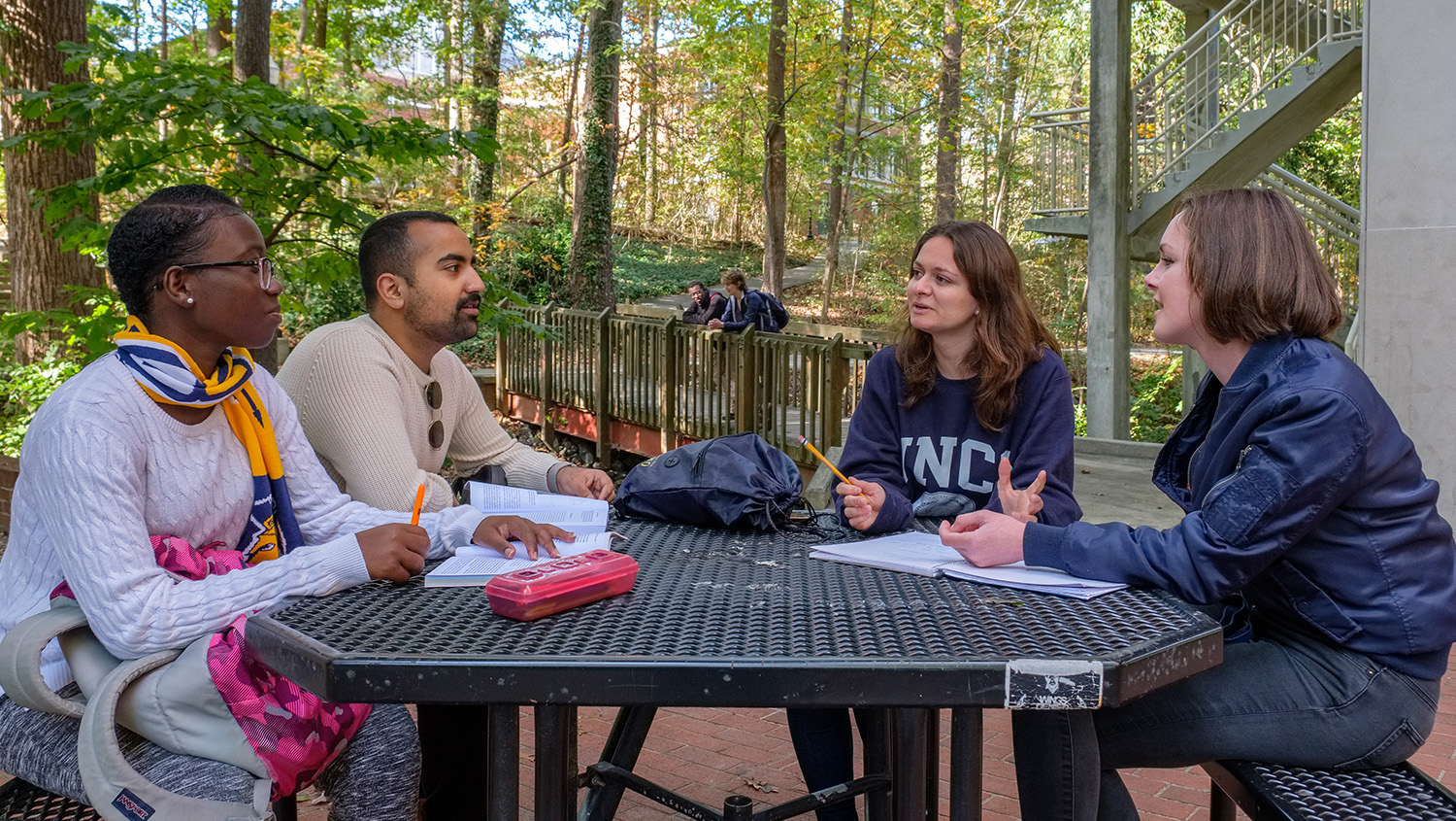 Four UNCG students sitting around outdoor picnic table with notebooks