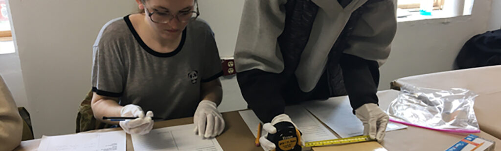 Two students behind a desk work to preserve and document artworks.