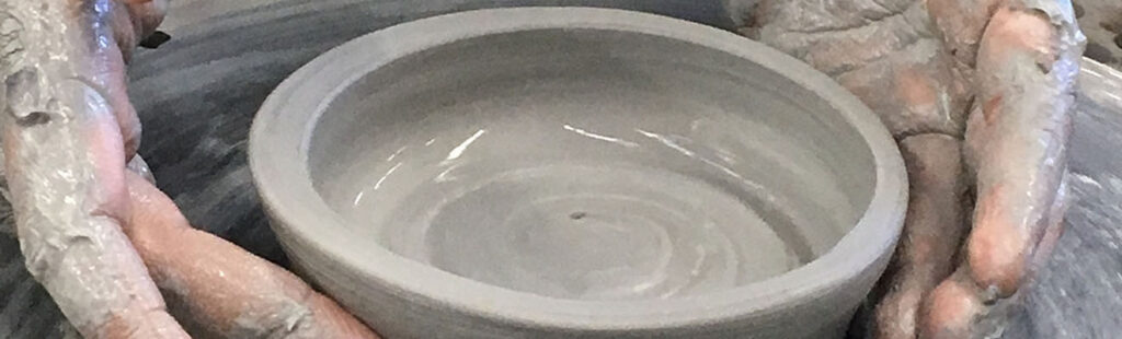 Hands spinning clay to create a ceramic piece on a wheel.