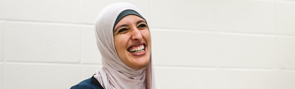 A UNCG student is sitting in a classroom. She is smiling and laughing, looking at an individual off camera to the right.