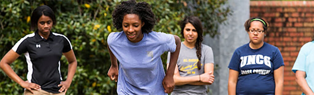 Kinesiology Graduate students stand and watch as another student runs forward.