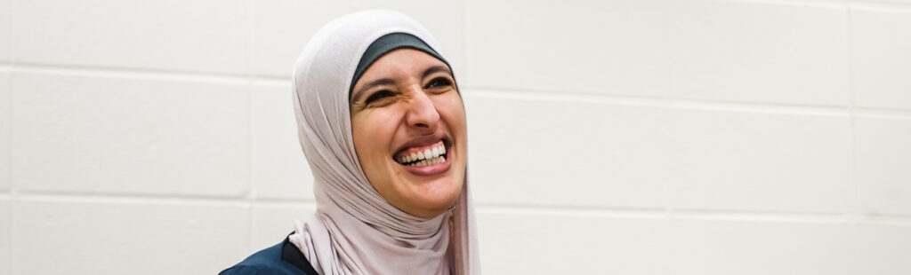 A UNCG student is sitting in a classroom. She is smiling and laughing, looking at an individual off camera to the right.