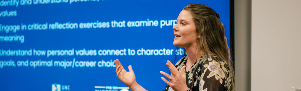 UNCG Bryan MS in IT and Management student presents during class. She is standing in front of a projector screen.