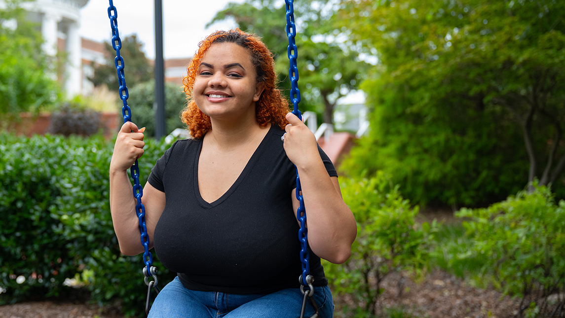A woman smiles and poses on a swing on campus.