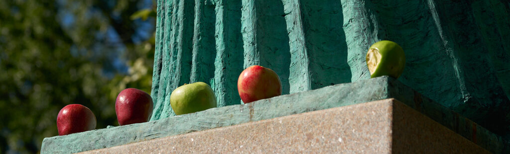 Five red and green apples sit at the bottom of the Statue of Minerva.