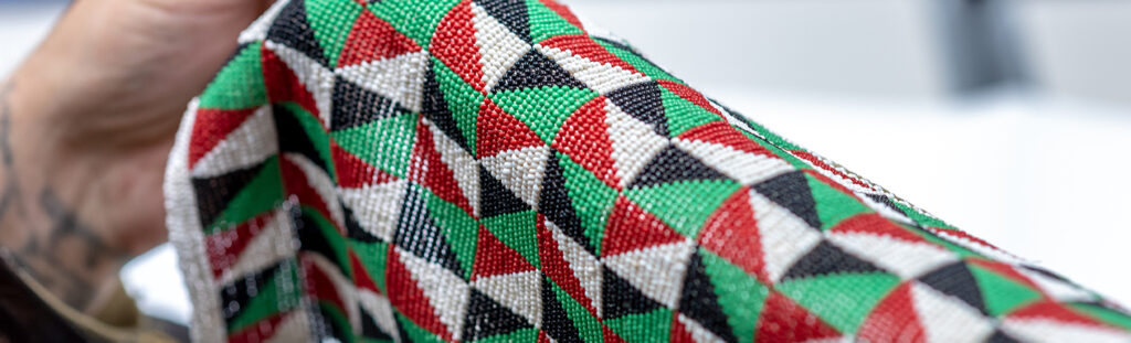 A student studying African American and African Diaspora culture holds a piece of woven fabric with a pattern of red, green, black, and white triangles