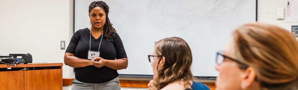 A teacher addresses students from the front of a classroom.