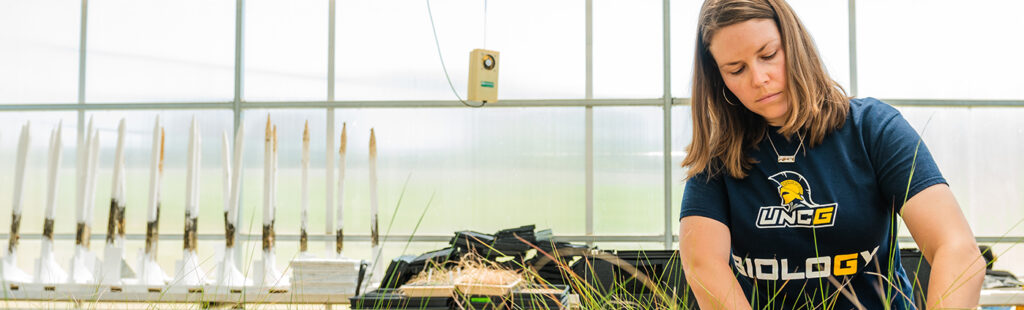 A female Bachelor's in Biology student inside a greenhouse at UNC Greensboro works with plants.