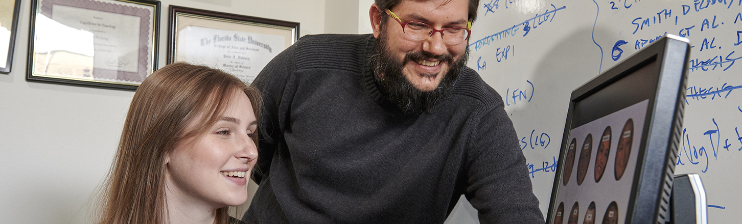 Two people look at a computer screen studying facial expressions.